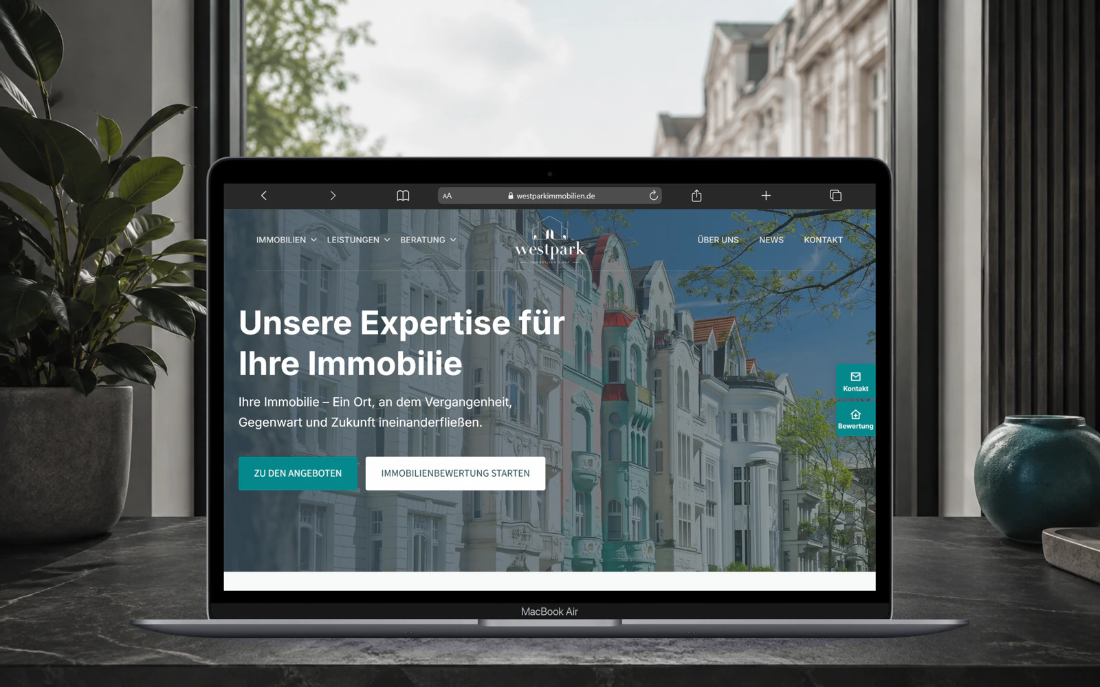 Notebook auf einem Schreibtisch mit der Startseite von Westpark Immobilien; im Hintergrund eine Straße mit Altbauten