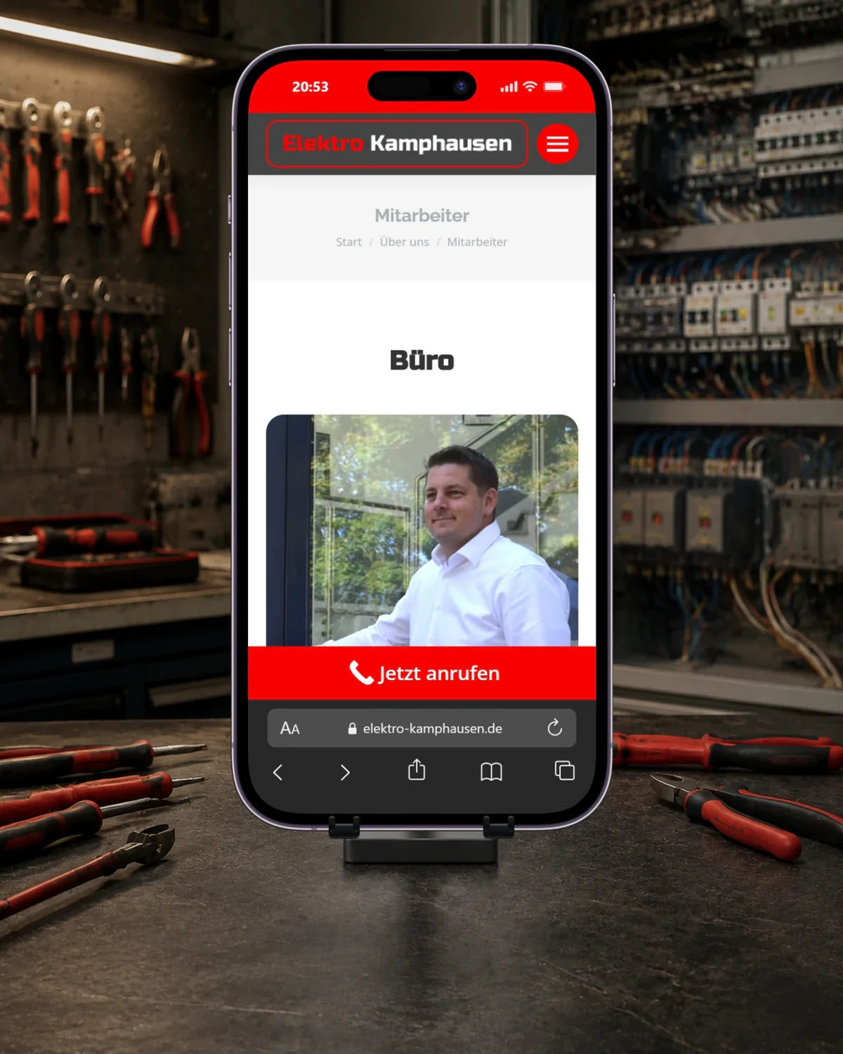 Smartphone mit der Kamphausen-Mitarbeiterseite, einem Mitarbeiterporträt und mobilem Telefonkontakt auf einer Werkbank