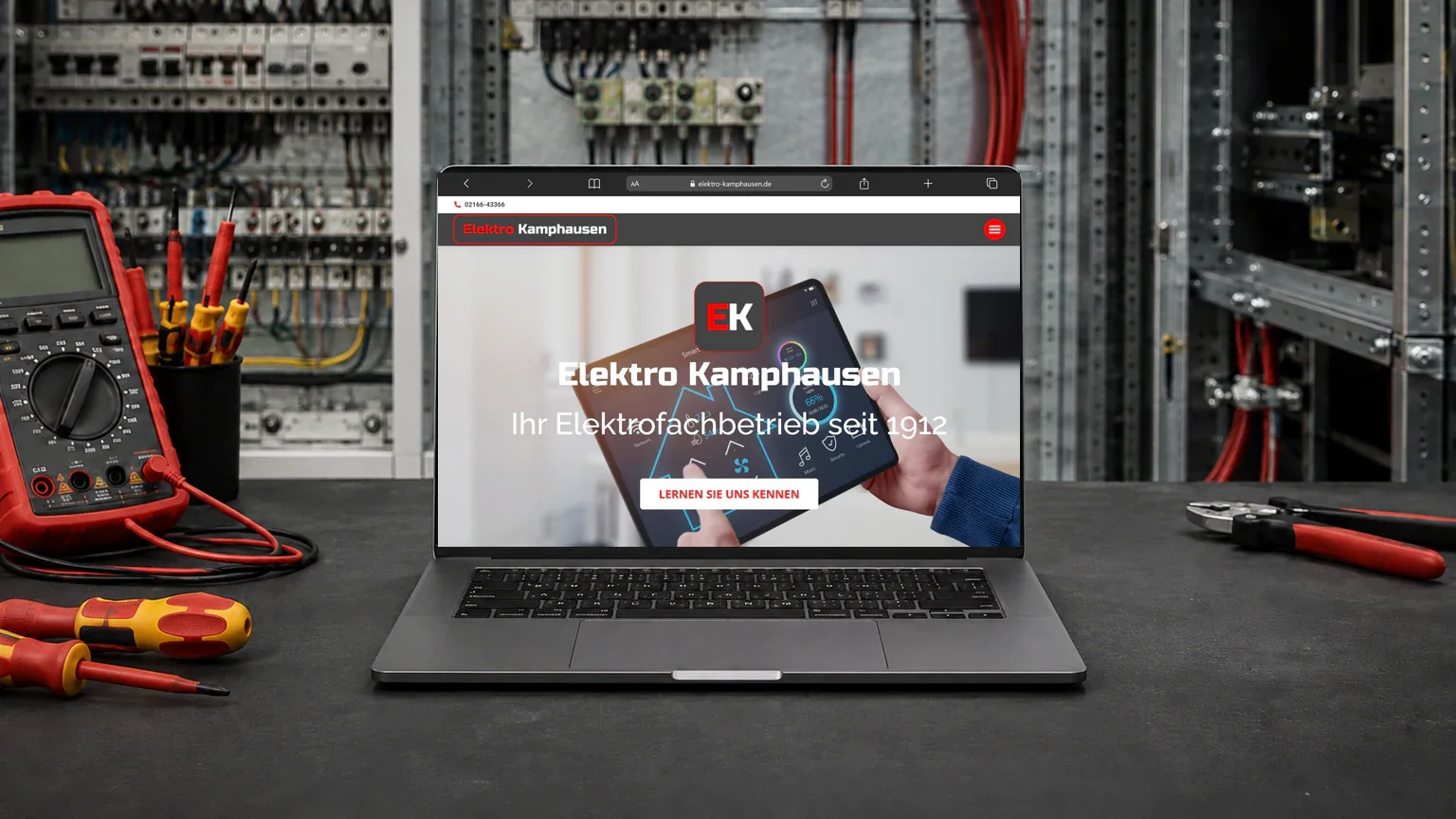 Laptop mit der Kamphausen-Website und Smart-Home-Motiv auf einer Werkbank vor einem geöffneten Schaltschrank
