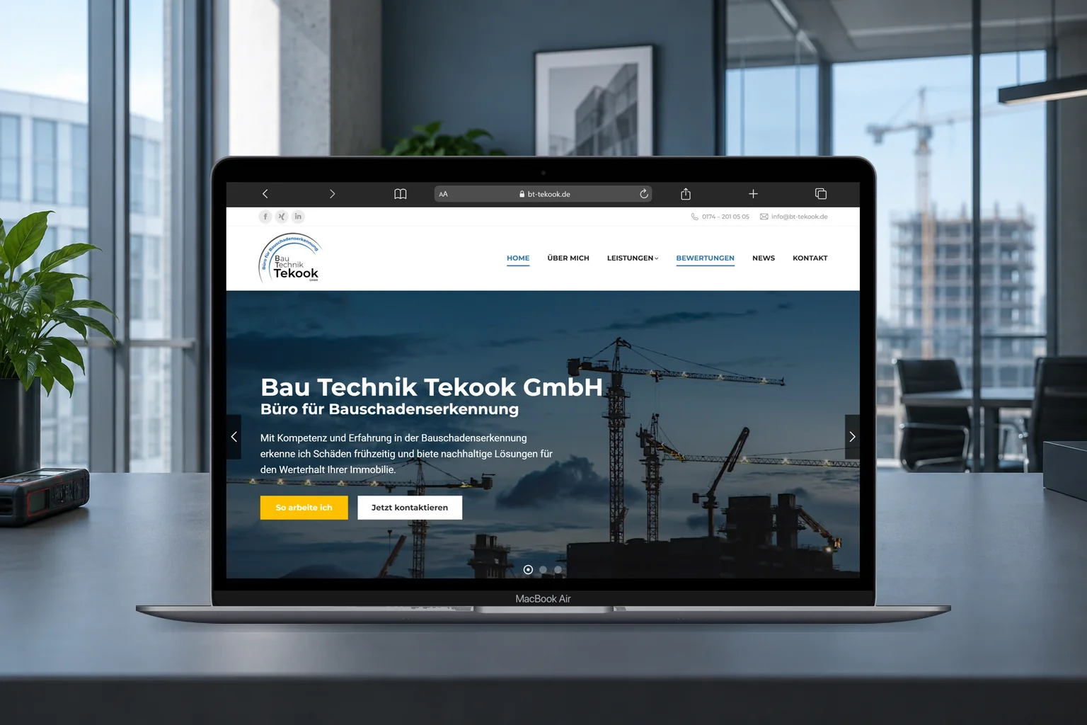 Website von Bau Technik Tekook auf einem MacBook Air in einem Büro mit Blick auf eine Baustelle