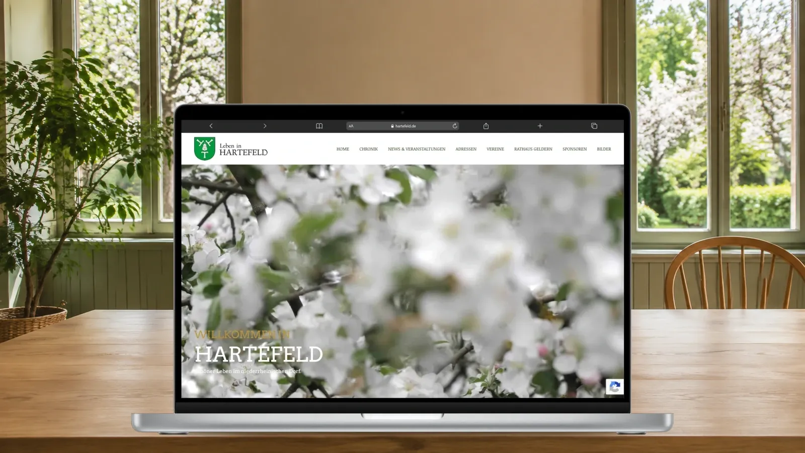 MacBook Pro mit der Hartefeld-Startseite in einem hellen Gemeinschaftsraum mit Blick ins Grüne