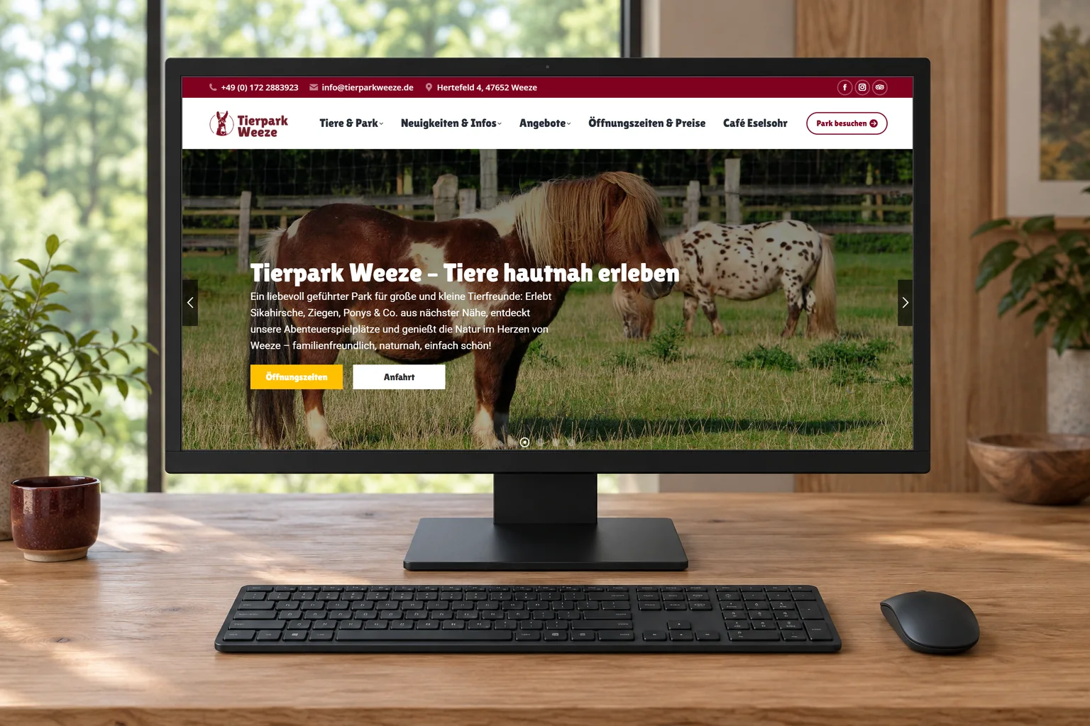 Startseite des Tierparks Weeze mit Ponys auf einem Desktopmonitor, davor Tastatur und Maus auf einem Holztisch.