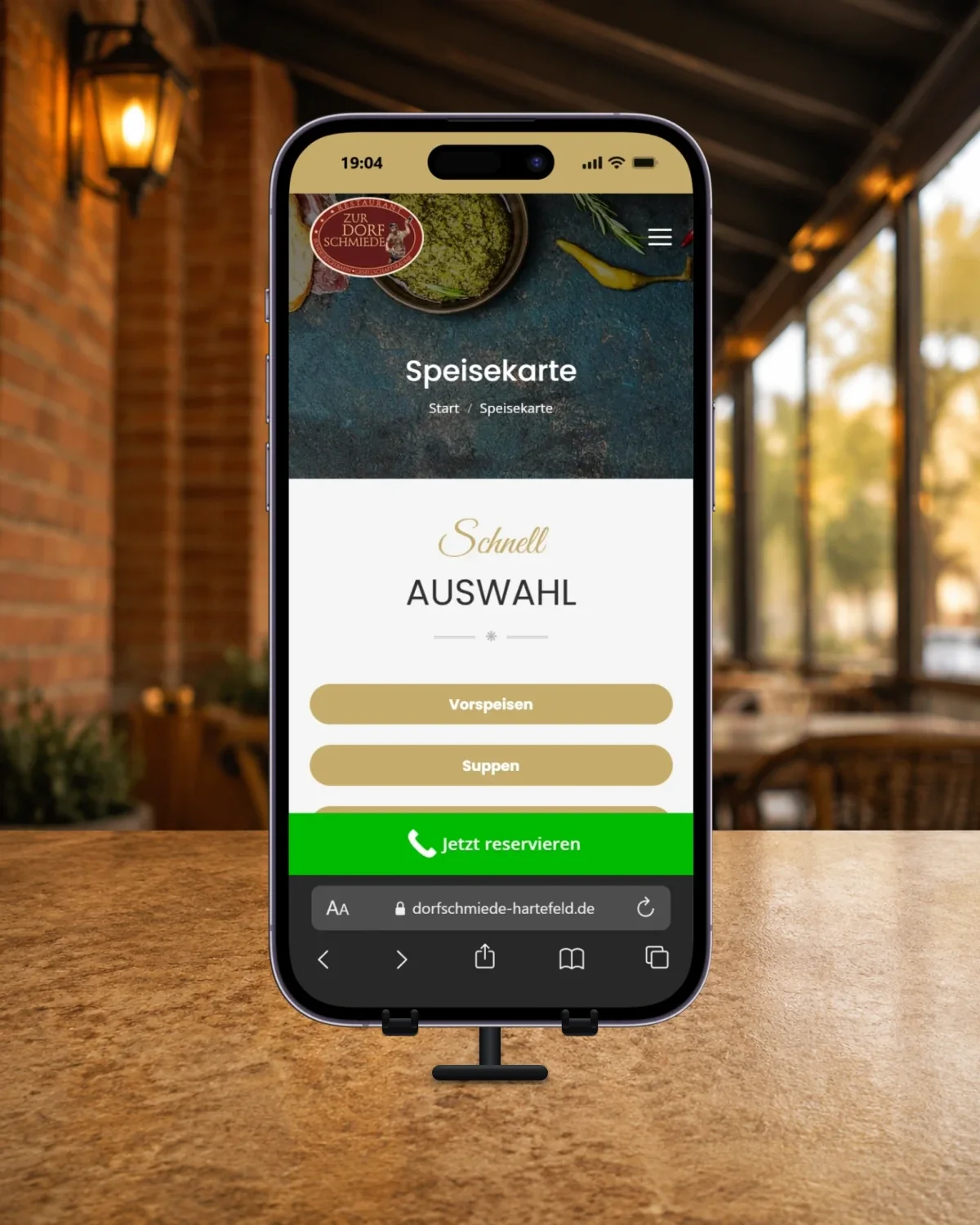 iPhone 14 Pro auf einem Tischständer vor einer unscharfen überdachten Terrasse; geöffnet ist die Speisekarte der Dorfschmiede Hartefeld.