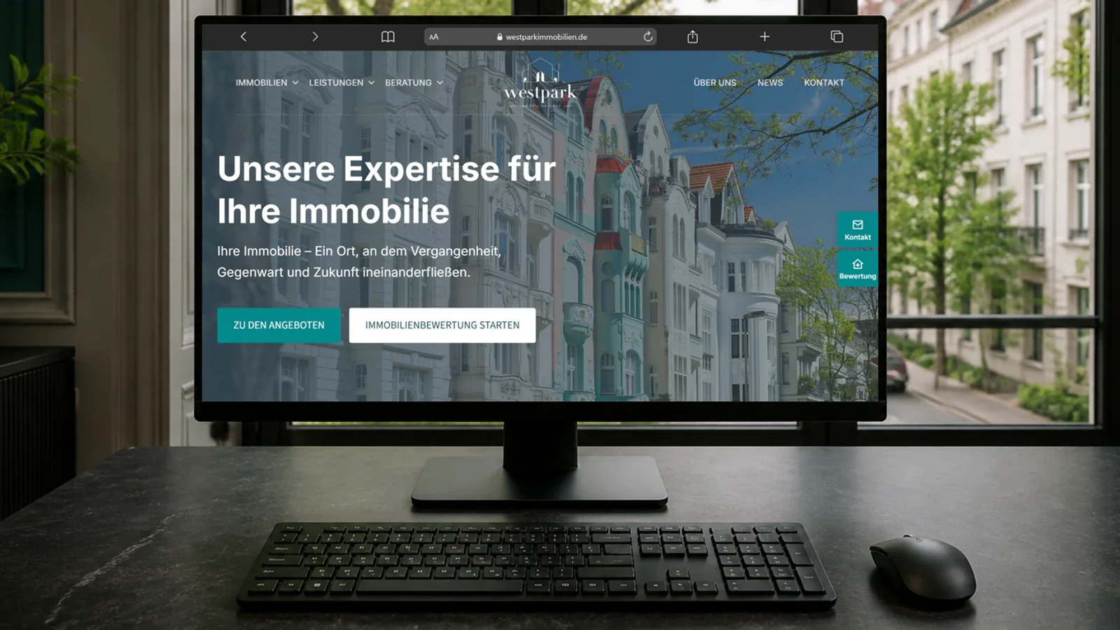 Website von Westpark Immobilien auf einem Monitor mit Tastatur und Maus vor einem Fenster mit Blick auf eine begrünte Altbaustraße
